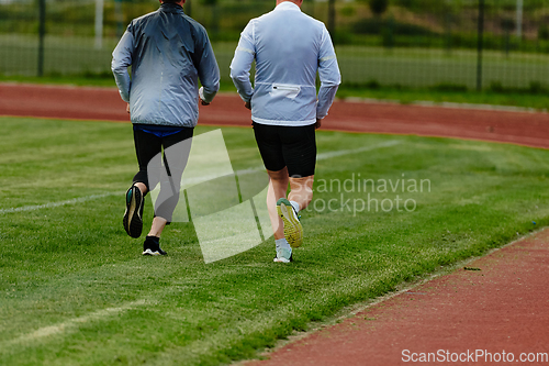 Image of An inspiring and active elderly couple showcase their dedication to fitness as they running together on a lush green field, captured in a close-up shot of their legs in motion.