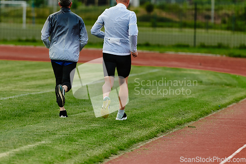 Image of An inspiring and active elderly couple showcase their dedication to fitness as they running together on a lush green field, captured in a close-up shot of their legs in motion.