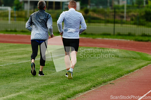 Image of An inspiring and active elderly couple showcase their dedication to fitness as they running together on a lush green field, captured in a close-up shot of their legs in motion.