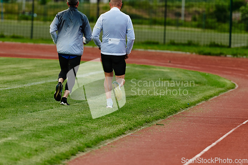 Image of An inspiring and active elderly couple showcase their dedication to fitness as they running together on a lush green field, captured in a close-up shot of their legs in motion.