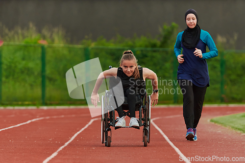 Image of A Muslim woman in a burqa running together with a woman in a wheelchair on the marathon course, preparing for future competitions.