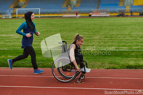 Image of A Muslim woman in a burqa running together with a woman in a wheelchair on the marathon course, preparing for future competitions.