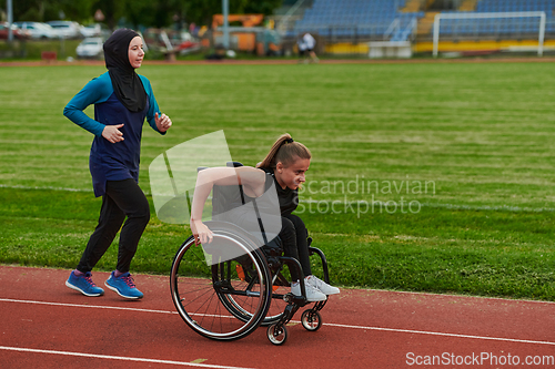 Image of A Muslim woman in a burqa running together with a woman in a wheelchair on the marathon course, preparing for future competitions.