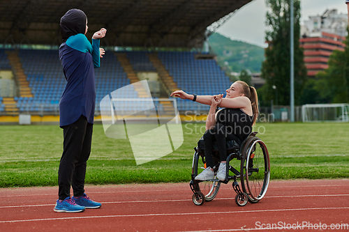 Image of Two strong and inspiring women, one Muslim in a burka and the other in a wheelchair stretching necks while on the marathon course