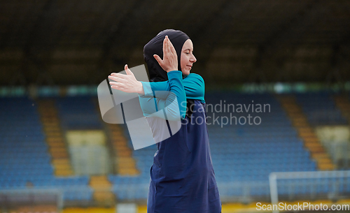 Image of A Muslim woman in a burqa, an Islamic sports outfit, is doing body exercises, stretching her neck, legs and back after a hard training session on the marathon course.