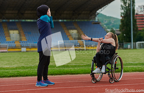 Image of Two strong and inspiring women, one a Muslim wearing a burka and the other in a wheelchair stretching and preparing their bodies for a marathon race on the track