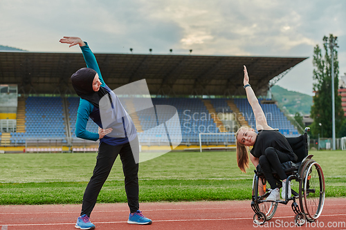 Image of Two strong and inspiring women, one a Muslim wearing a burka and the other in a wheelchair stretching and preparing their bodies for a marathon race on the track