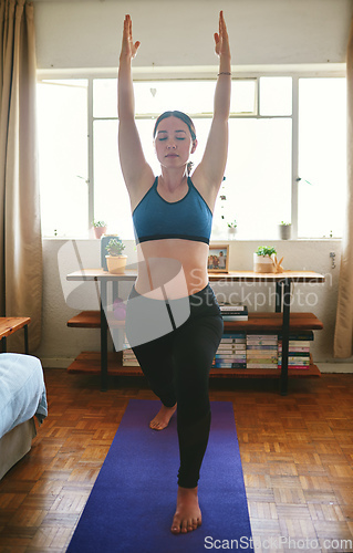 Image of They say no pain, no gain. Cropped shot of an attractive young woman standing and holding a warrior pose while doing yoga in her home.