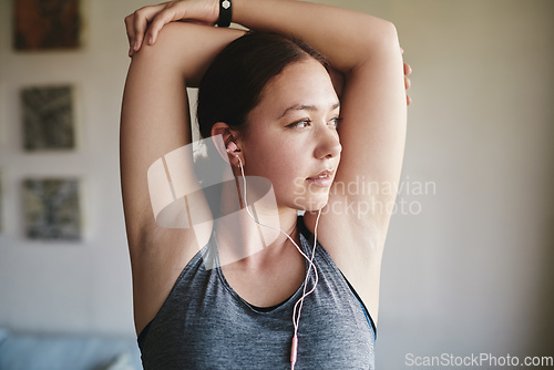 Image of I always stretch before and after a workout. Cropped shot of an attractive young woman standing in her room and stretching her tricep after a workout at home.