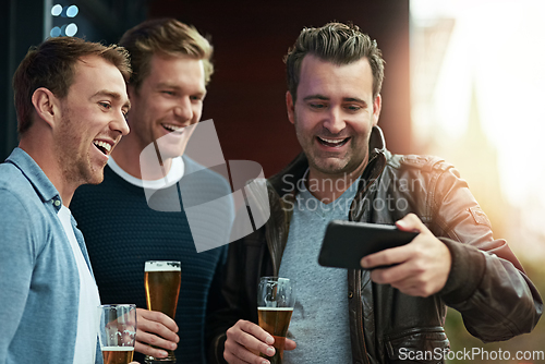 Image of Check out this video. Shot of a group of friends enjoying a beer together while standing on a balcony together.