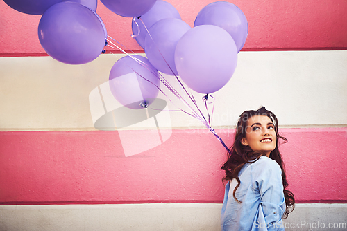 Image of Having colourful fun in the city. Cropped shot of a beautiful young woman holding purple balloons against a wall outside.