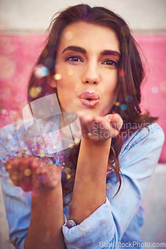 Image of Be the sparkle you want to see. Portrait of a beautiful young woman blowing confetti outside.