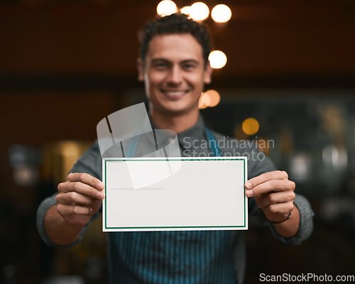 Image of We will be glad if you can join us. Portrait of a cheerful young man holding a sign while standing inside of a beer brewery during the day.