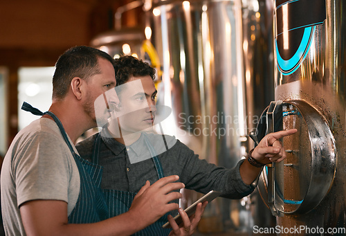 Image of Is this container cold enough. Shot of two young working men doing inspection of their beer making machinery inside of a beer brewery during the day.