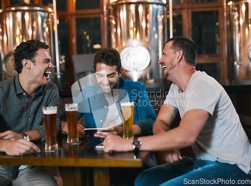 Image of Time to talk business over a beer. Shot of three cheerful young men drinking beer together at a table inside of a beer brewery during the day.