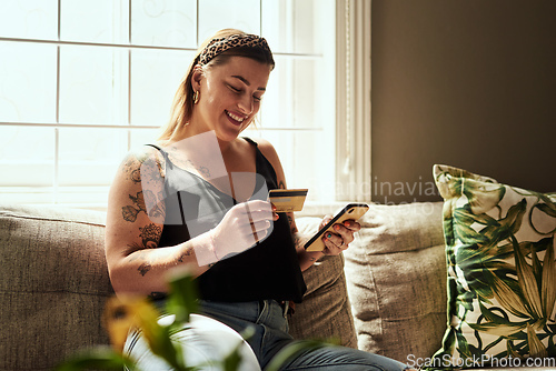 Image of Shopping day minus the queues. Shot of a young woman using a smartphone and credit card on the sofa at home.