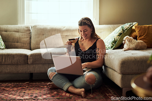 Image of Less queues more relaxing. Shot of a young woman using a laptop and credit card in her living room at home.