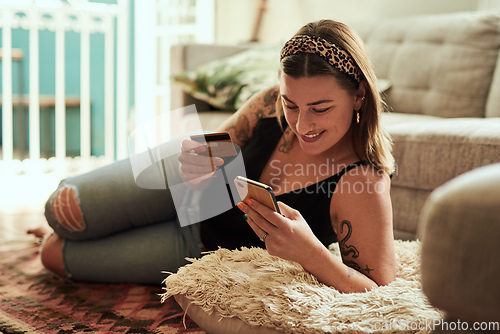 Image of Shopping just gets easier and easier. Shot of a young woman using a smartphone and credit card in her living room at home.