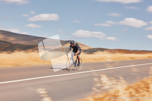 Image of Road, nature and man cycling fast for workout, exercise and scenic mountain path with motion. Health, wellness and cyclist on speed bike for morning training, practice and bicycle race with blue sky.