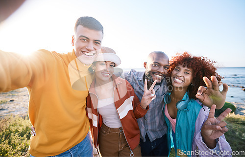 Image of Selfie, happy and portrait of friends by the beach on summer vacation, adventure or weekend trip. Smile, diversity and young people having fun and taking picture with peace sign by ocean on holiday.