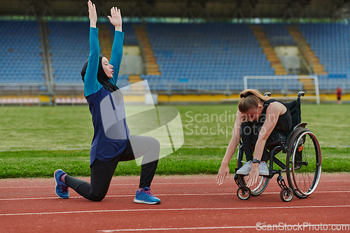 Image of Two strong and inspiring women, one a Muslim wearing a burka and the other in a wheelchair stretching and preparing their bodies for a marathon race on the track