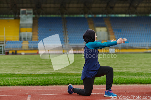 Image of A Muslim woman in a burqa, an Islamic sports outfit, is doing body exercises, stretching her neck, legs and back after a hard training session on the marathon course.