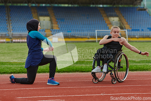 Image of Two strong and inspiring women, one a Muslim wearing a burka and the other in a wheelchair stretching and preparing their bodies for a marathon race on the track