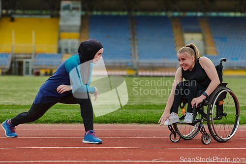 Image of Two strong and inspiring women, one a Muslim wearing a burka and the other in a wheelchair stretching and preparing their bodies for a marathon race on the track