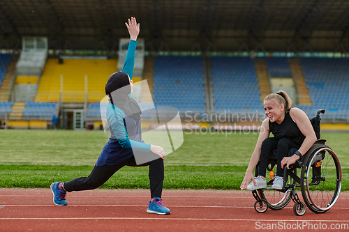 Image of Two strong and inspiring women, one a Muslim wearing a burka and the other in a wheelchair stretching and preparing their bodies for a marathon race on the track