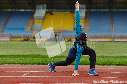 Image of A Muslim woman in a burqa, an Islamic sports outfit, is doing body exercises, stretching her neck, legs and back after a hard training session on the marathon course.