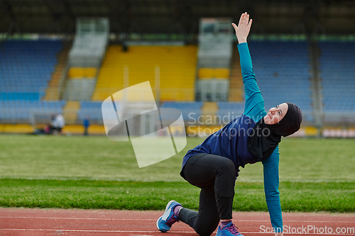 Image of A Muslim woman in a burqa, an Islamic sports outfit, is doing body exercises, stretching her neck, legs and back after a hard training session on the marathon course.