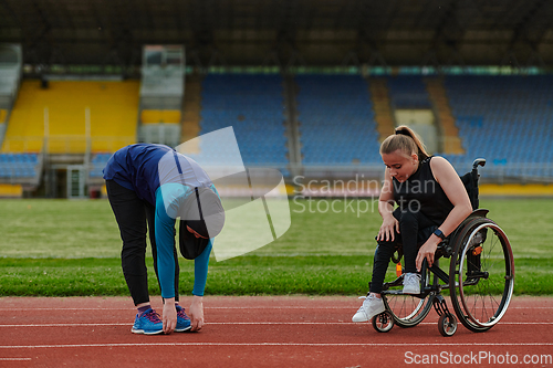 Image of Two strong and inspiring women, one a Muslim wearing a burka and the other in a wheelchair stretching and preparing their bodies for a marathon race on the track