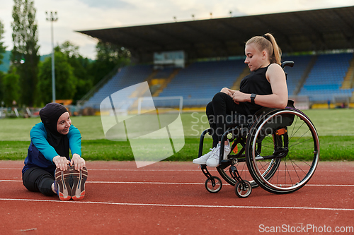 Image of Two strong and inspiring women, one a Muslim wearing a burka and the other in a wheelchair stretching and preparing their bodies for a marathon race on the track