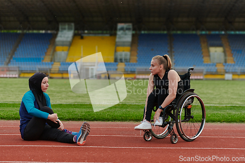 Image of Two strong and inspiring women, one a Muslim wearing a burka and the other in a wheelchair stretching and preparing their bodies for a marathon race on the track