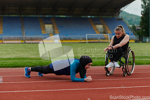 Image of Two strong and inspiring women, one a Muslim wearing a burka and the other in a wheelchair stretching and preparing their bodies for a marathon race on the track