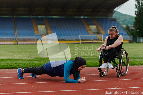 Image of Two strong and inspiring women, one a Muslim wearing a burka and the other in a wheelchair stretching and preparing their bodies for a marathon race on the track