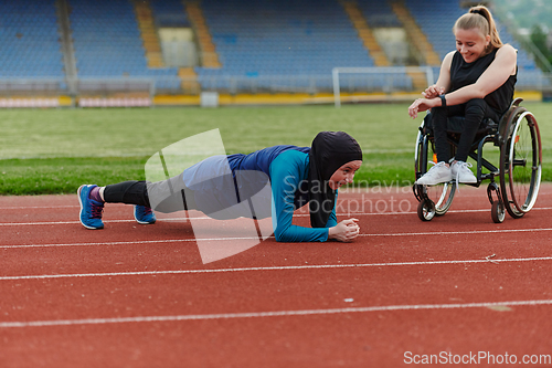 Image of Two strong and inspiring women, one a Muslim wearing a burka and the other in a wheelchair stretching and preparing their bodies for a marathon race on the track