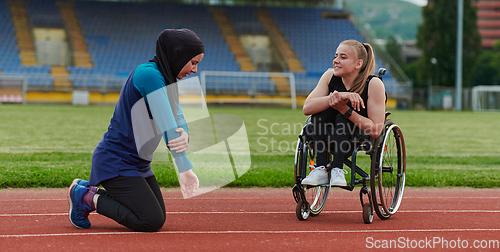 Image of Two strong and inspiring women, one a Muslim wearing a burka and the other in a wheelchair stretching and preparing their bodies for a marathon race on the track