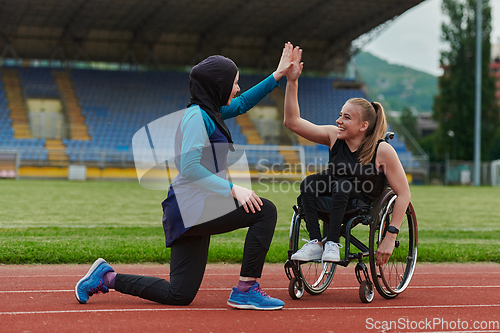 Image of Two strong and inspiring women, one a Muslim wearing a burka and the other in a wheelchair stretching and preparing their bodies for a marathon race on the track