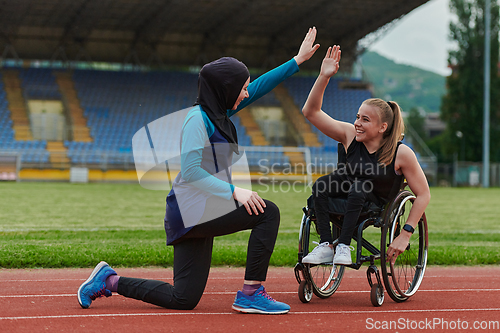 Image of Two strong and inspiring women, one a Muslim wearing a burka and the other in a wheelchair stretching and preparing their bodies for a marathon race on the track