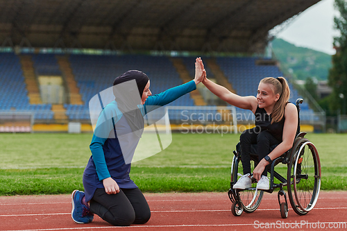 Image of A Muslim woman wearing a burqa supports her friend with disability in a wheelchair as they train together on a marathon course.