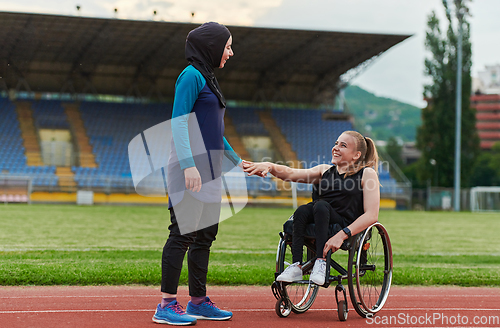 Image of A Muslim woman wearing a burqa supports her friend with disability in a wheelchair as they train together on a marathon course.