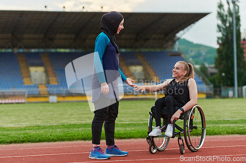 Image of A Muslim woman wearing a burqa supports her friend with disability in a wheelchair as they train together on a marathon course.