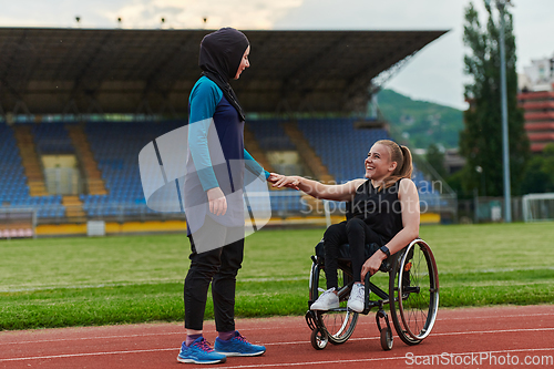 Image of A Muslim woman wearing a burqa supports her friend with disability in a wheelchair as they train together on a marathon course.