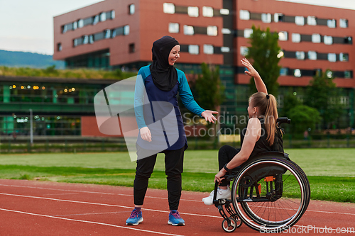 Image of A Muslim woman wearing a burqa supports her friend with disability in a wheelchair as they train together on a marathon course.