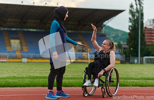 Image of A Muslim woman wearing a burqa supports her friend with disability in a wheelchair as they train together on a marathon course.