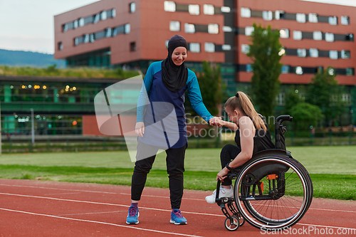 Image of A Muslim woman wearing a burqa supports her friend with disability in a wheelchair as they train together on a marathon course.