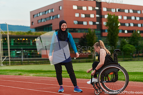 Image of A Muslim woman wearing a burqa supports her friend with disability in a wheelchair as they train together on a marathon course.