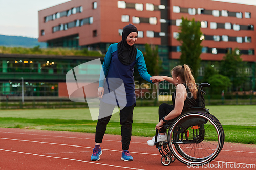 Image of A Muslim woman wearing a burqa supports her friend with disability in a wheelchair as they train together on a marathon course.