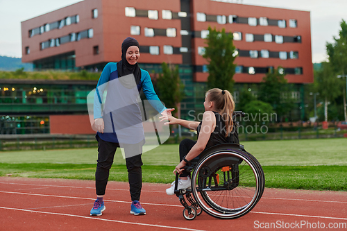 Image of A Muslim woman wearing a burqa supports her friend with disability in a wheelchair as they train together on a marathon course.